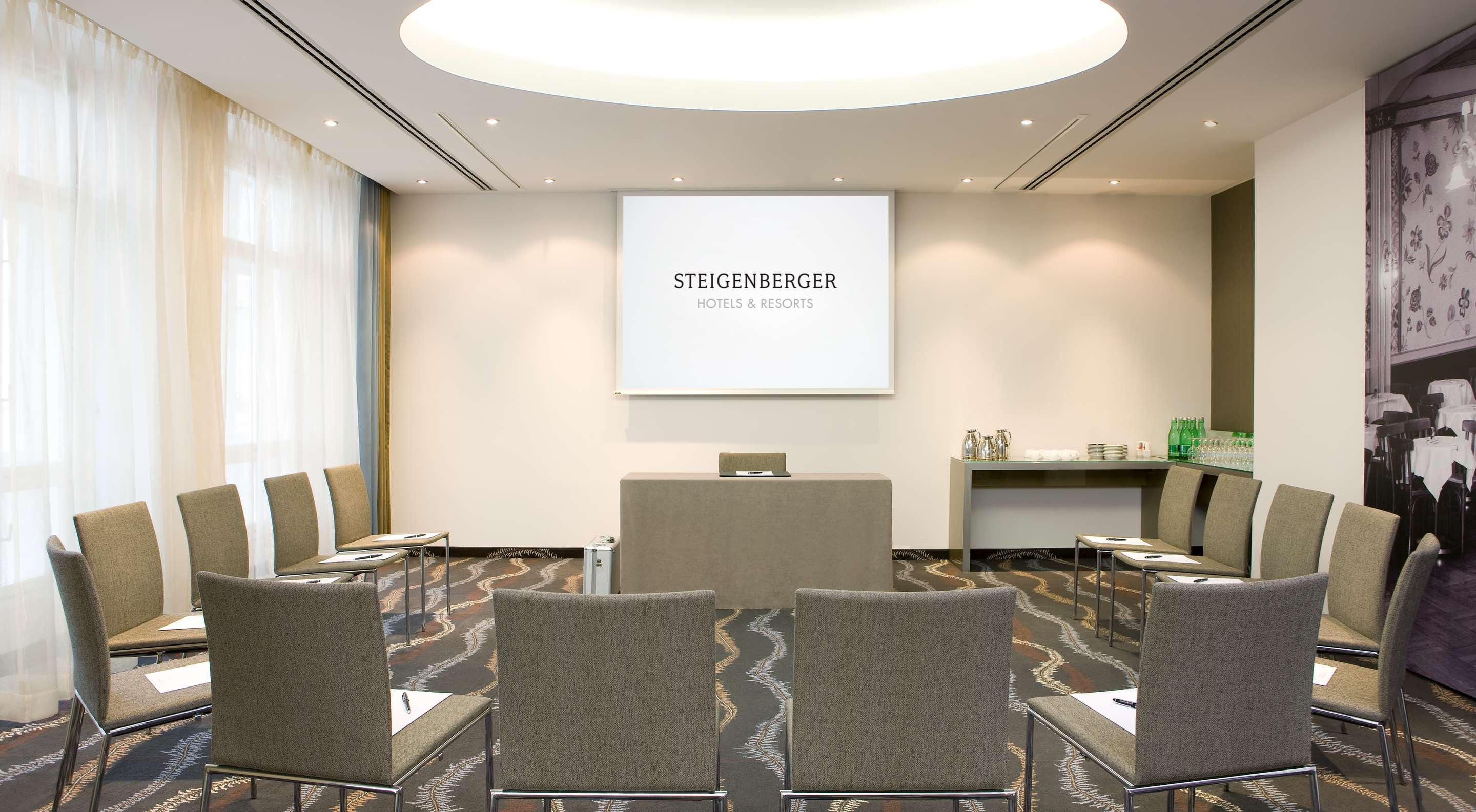 Steigenberger Hotel Herrenhof Vienna Exterior photo The photo shows a meeting room or conference space. There are several chairs arranged in a semi-circle facing a presentation screen that displays the name "Steigenberger Hotels & Resorts." In front of the screen, there is a small table that likely ho