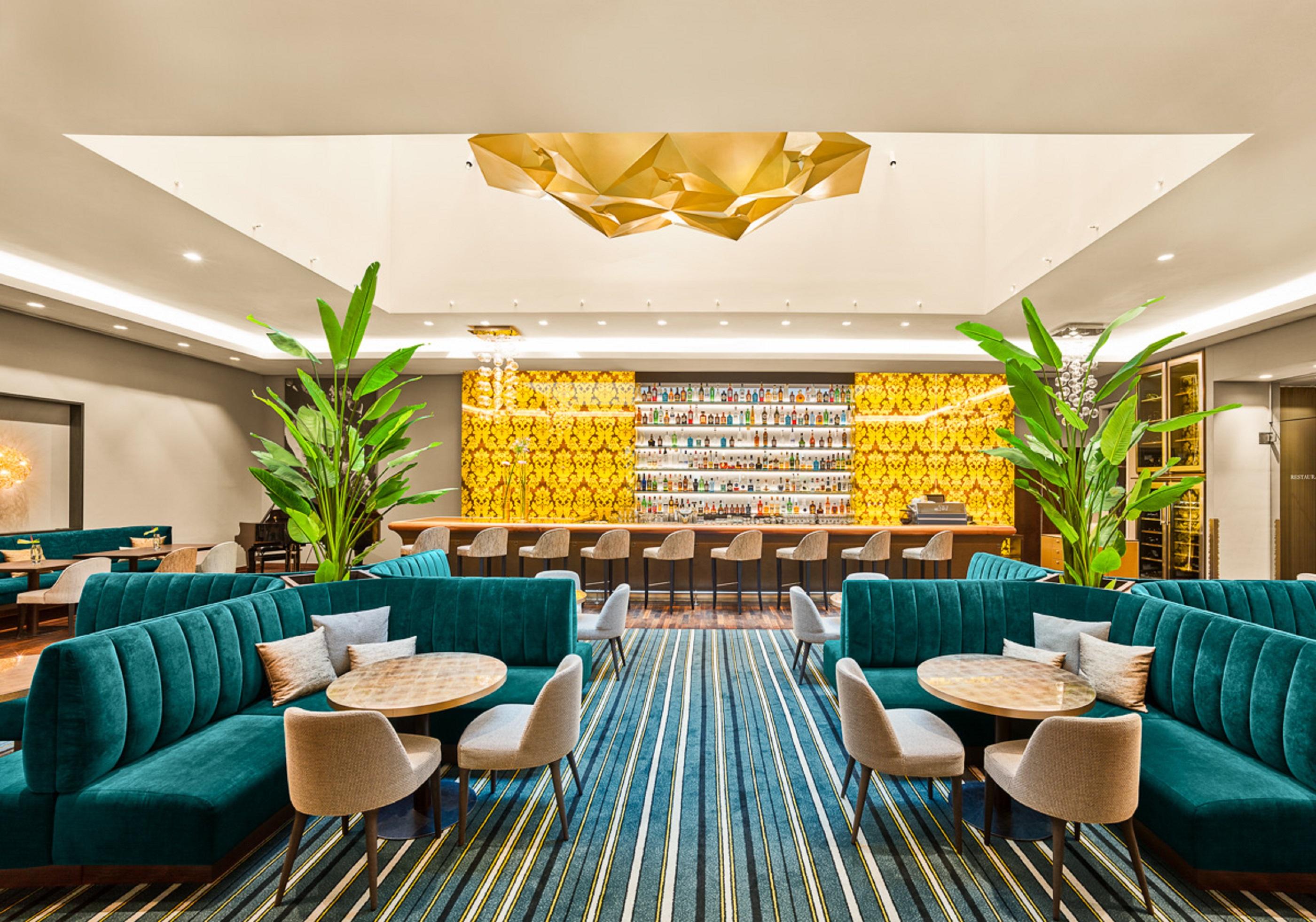 Steigenberger Hotel Herrenhof Vienna Exterior photo The photo shows a modern lounge or bar area featuring stylish teal seating arrangements, including plush sofas and round tables. In the background, there is a well-lit bar decorated with a vibrant yellow wall, adorned with various bottles. The space 