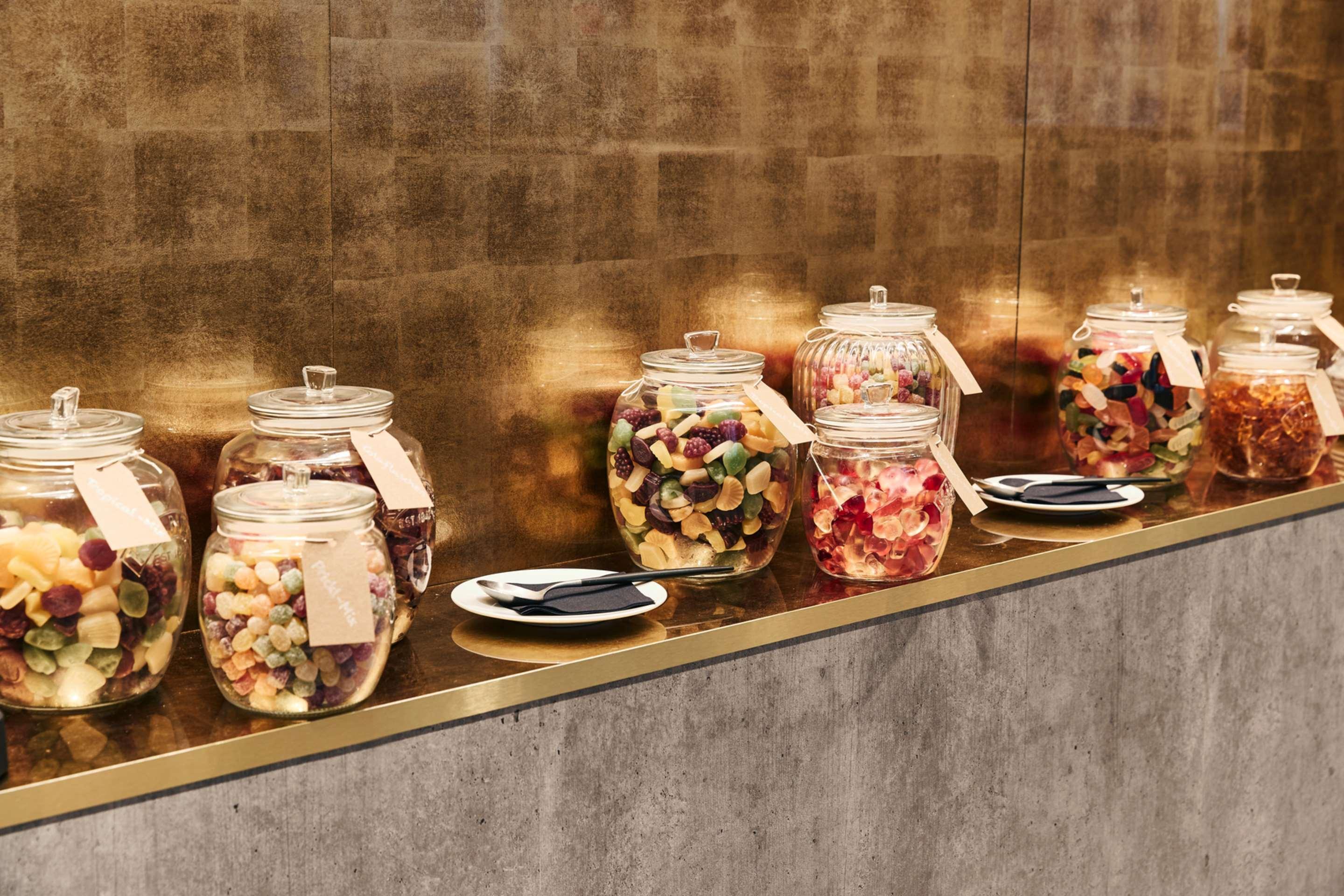 Steigenberger Hotel Herrenhof Vienna Exterior photo The photo shows a display of several glass jars filled with various types of candy. Each jar is labeled and positioned on a sleek, horizontal surface against a golden background. There are some small plates placed in front of the jars, which likely c