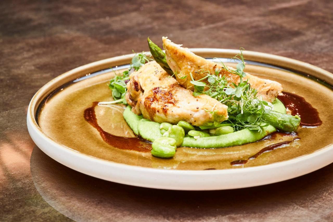 Steigenberger Hotel Herrenhof Vienna Exterior photo The photo showcases a plated dish featuring grilled chicken fillets, served on a bed of smooth green puree, likely made from peas or avocado. Accompanying the chicken are fresh green pea shoots and asparagus, adding vibrant colors and textures. A dri