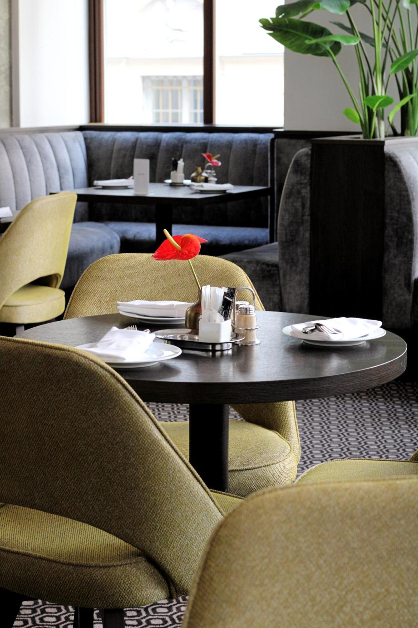Steigenberger Hotel Herrenhof Vienna Exterior photo The photo shows a stylish restaurant interior featuring a table set for dining. The table has two plates, cutlery, and small condiment containers neatly arranged. A decorative red flower, possibly a cocktail garnish, stands in a holder at the center 